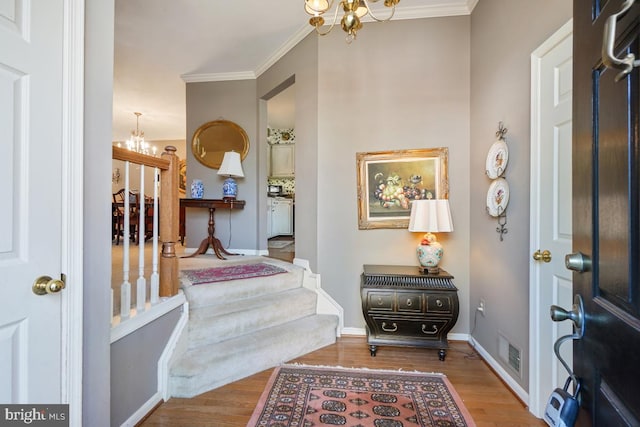 entryway with visible vents, wood finished floors, an inviting chandelier, crown molding, and baseboards