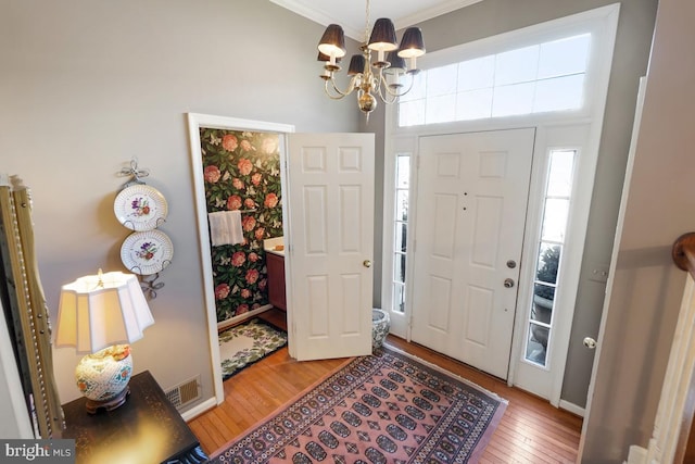 entrance foyer featuring visible vents, hardwood / wood-style flooring, an inviting chandelier, crown molding, and baseboards