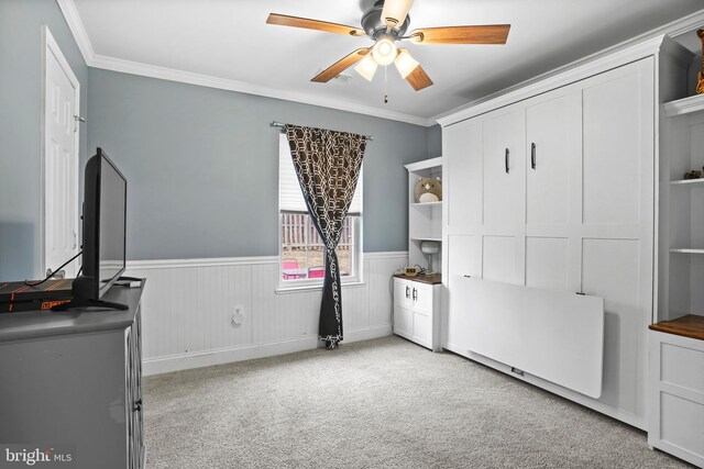 interior space featuring ceiling fan, light colored carpet, ornamental molding, and wainscoting