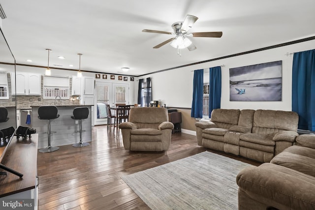 living room featuring dark wood-style floors, baseboards, ceiling fan, and ornamental molding