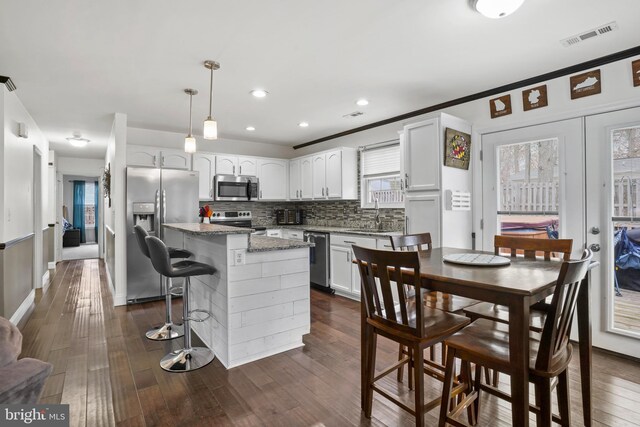 kitchen with visible vents, a kitchen island, decorative backsplash, appliances with stainless steel finishes, and dark wood-style flooring