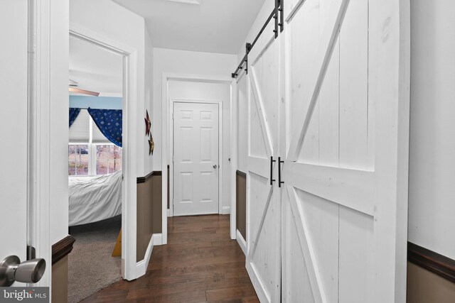 hall with baseboards, a barn door, and dark wood-style flooring