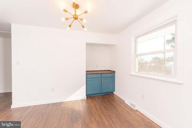 unfurnished room with visible vents, baseboards, an inviting chandelier, and wood finished floors