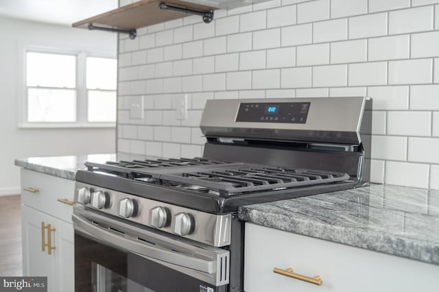 kitchen with decorative backsplash, white cabinetry, stainless steel gas range, and light stone countertops