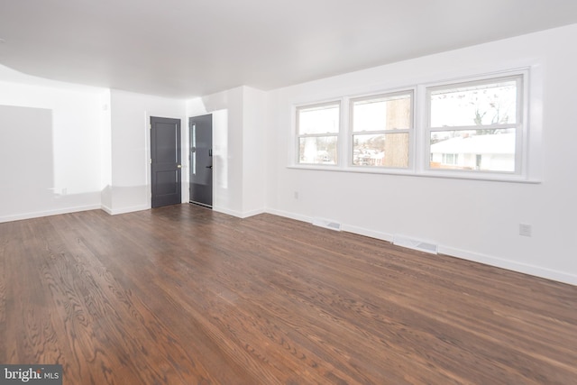 empty room featuring visible vents, baseboards, and dark wood-style floors