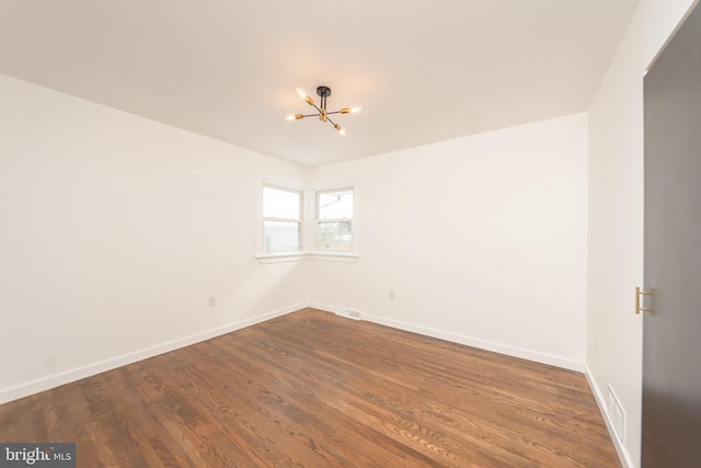 empty room featuring an inviting chandelier, baseboards, dark wood-style flooring, and visible vents