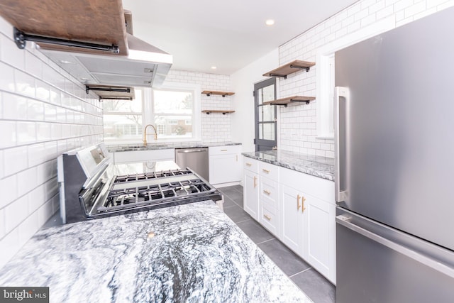 kitchen with light stone countertops, decorative backsplash, stainless steel appliances, white cabinetry, and open shelves