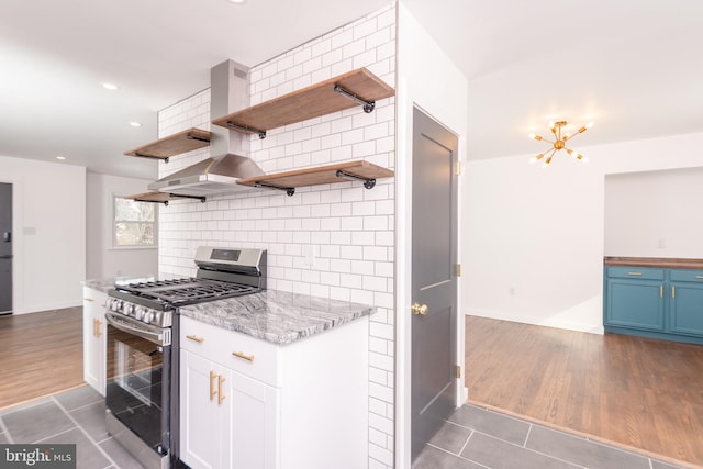 kitchen featuring tasteful backsplash, blue cabinets, gas range, wall chimney exhaust hood, and open shelves