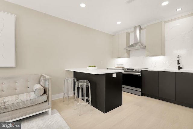 kitchen featuring a breakfast bar area, dark cabinetry, electric range, wall chimney exhaust hood, and a sink