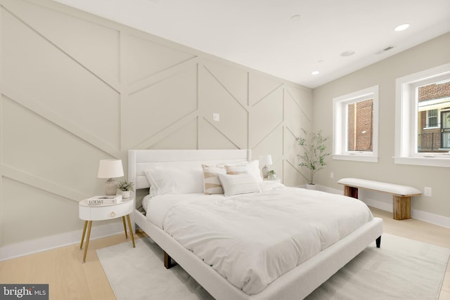 bedroom with light wood-type flooring, visible vents, recessed lighting, a decorative wall, and baseboards