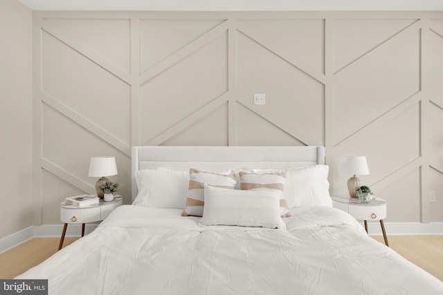 bedroom with a decorative wall, wood finished floors, and baseboards