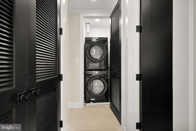 clothes washing area featuring laundry area, wood finished floors, crown molding, and stacked washer and clothes dryer