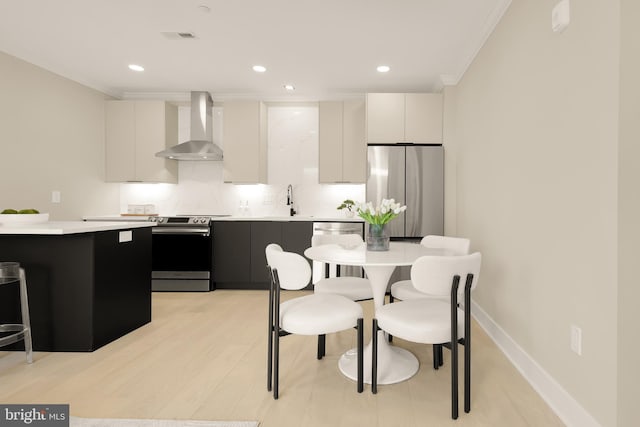 kitchen with wall chimney range hood, dark cabinetry, appliances with stainless steel finishes, light countertops, and baseboards