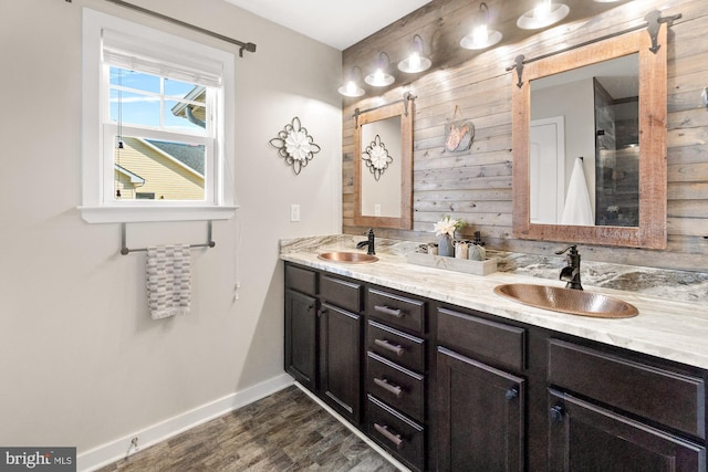 full bath featuring double vanity, wood finished floors, baseboards, and a sink