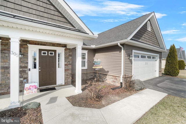 entrance to property featuring aphalt driveway, a garage, stone siding, and a shingled roof