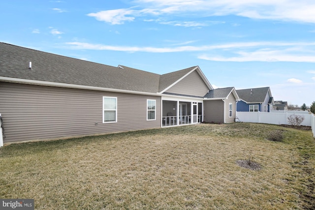 rear view of house with a sunroom, a lawn, roof with shingles, and fence