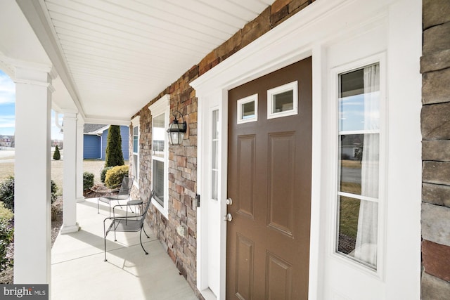 view of exterior entry with stone siding and a porch