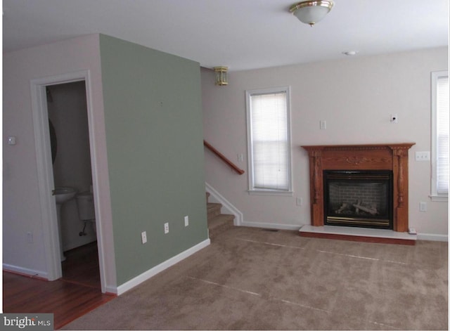 unfurnished living room with a glass covered fireplace, stairway, and baseboards