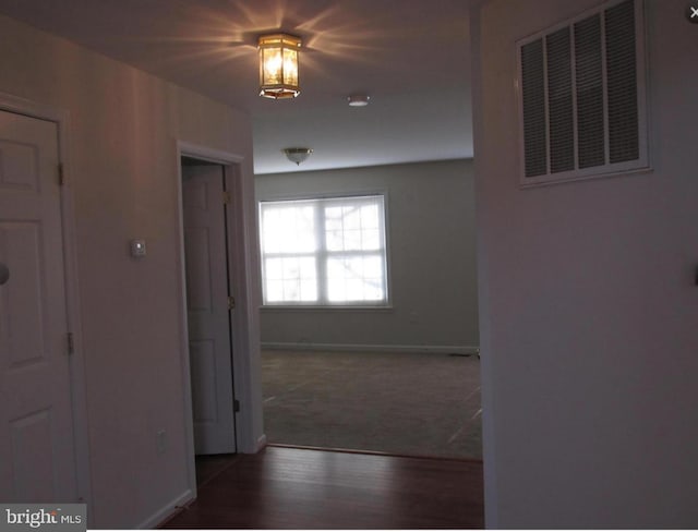 hallway featuring visible vents, baseboards, and wood finished floors