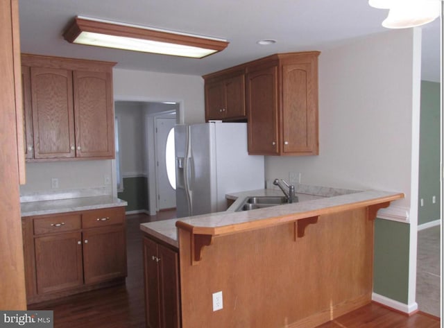 kitchen with a breakfast bar area, a peninsula, dark wood-style flooring, a sink, and white refrigerator with ice dispenser