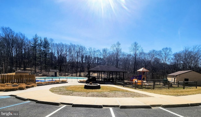 view of property's community with fence, playground community, a gazebo, a swimming pool, and uncovered parking