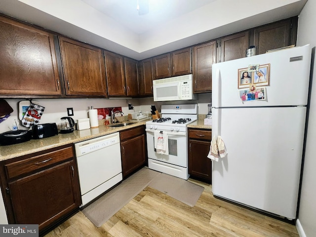 kitchen featuring dark brown cabinets, white appliances, light wood-type flooring, and a sink