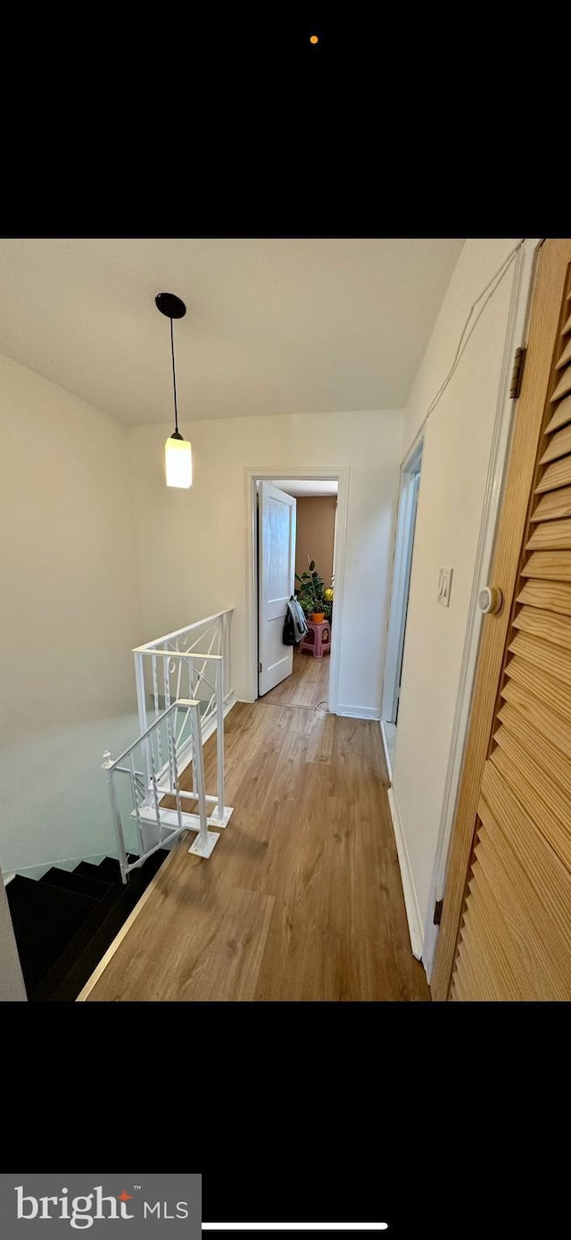 corridor featuring baseboards, an upstairs landing, and wood finished floors