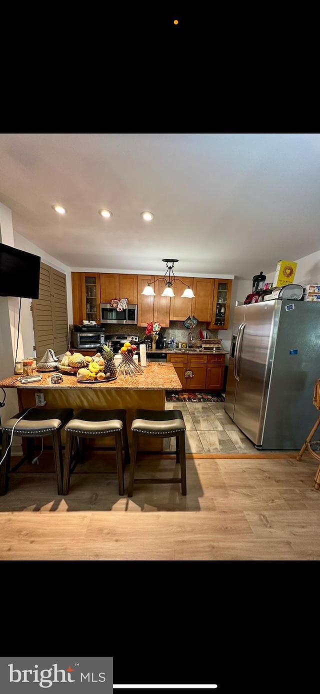 kitchen with light wood finished floors, recessed lighting, brown cabinets, appliances with stainless steel finishes, and a sink