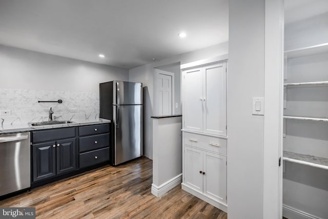 kitchen with wood finished floors, recessed lighting, a sink, decorative backsplash, and stainless steel appliances