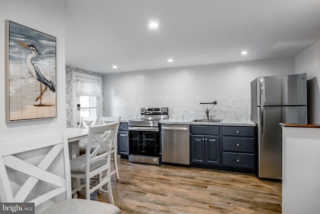 kitchen with wood finished floors, recessed lighting, a sink, decorative backsplash, and appliances with stainless steel finishes