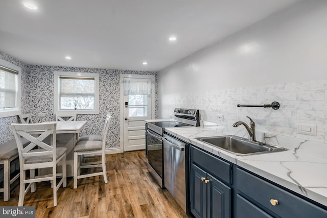 kitchen with blue cabinets, light wood-style flooring, a sink, appliances with stainless steel finishes, and wallpapered walls