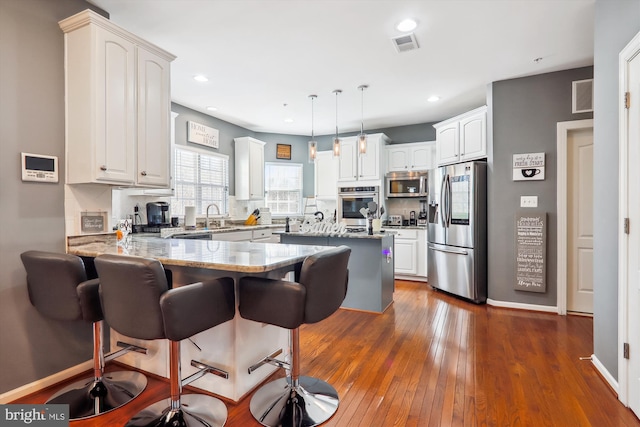 kitchen featuring a breakfast bar area, visible vents, a peninsula, stainless steel appliances, and white cabinetry