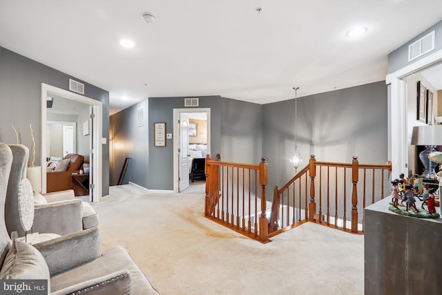 hall featuring visible vents, an upstairs landing, and light carpet