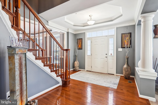 entrance foyer with a raised ceiling, hardwood / wood-style floors, ornamental molding, and ornate columns