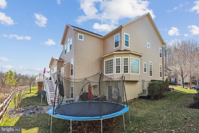 rear view of house featuring fence, a yard, stairs, a trampoline, and brick siding