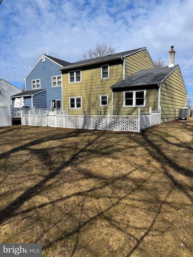 back of house with central AC unit, a chimney, and a yard