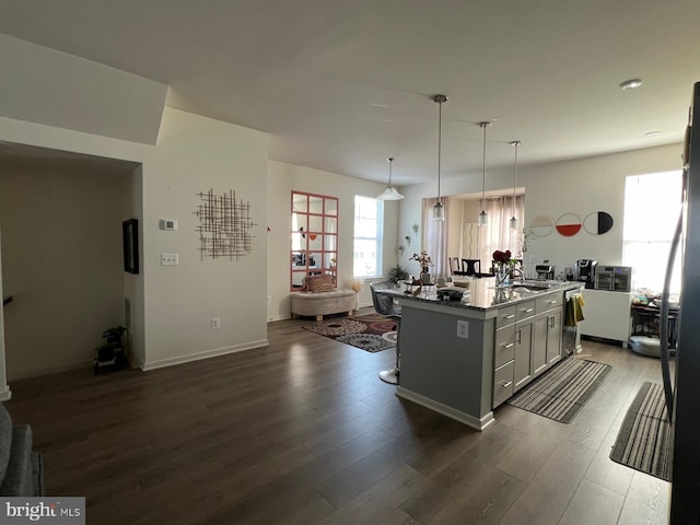 kitchen featuring dark wood-type flooring, decorative light fixtures, an island with sink, and open floor plan