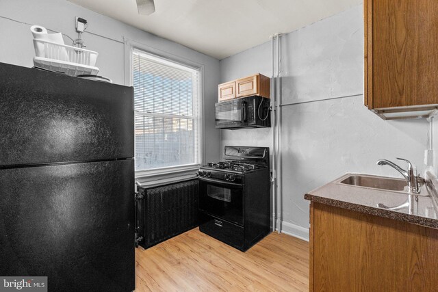 kitchen with radiator, a sink, black appliances, dark countertops, and light wood-type flooring