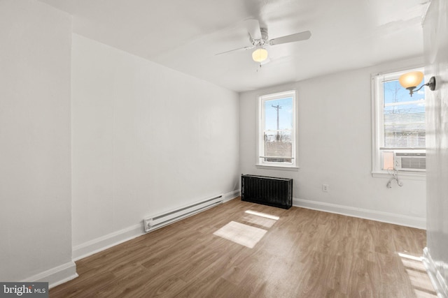 unfurnished room with baseboard heating, a healthy amount of sunlight, radiator, and wood finished floors