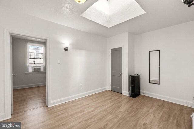 spare room featuring light wood-style flooring, a textured ceiling, a skylight, and baseboards