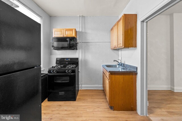 kitchen featuring light wood finished floors, black appliances, dark countertops, and a sink