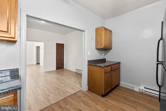 kitchen with dark countertops, brown cabinets, light wood-type flooring, and a baseboard radiator