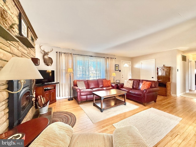 living area with a glass covered fireplace, light wood-style flooring, and visible vents