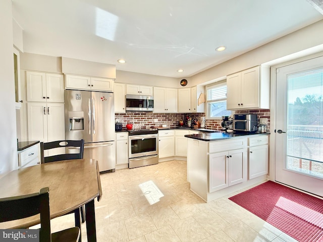 kitchen featuring a peninsula, stainless steel appliances, white cabinets, dark countertops, and tasteful backsplash