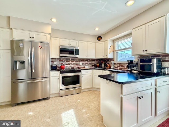 kitchen featuring dark countertops, stainless steel appliances, a peninsula, white cabinets, and decorative backsplash