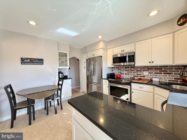 kitchen with a sink, dark stone countertops, arched walkways, appliances with stainless steel finishes, and decorative backsplash