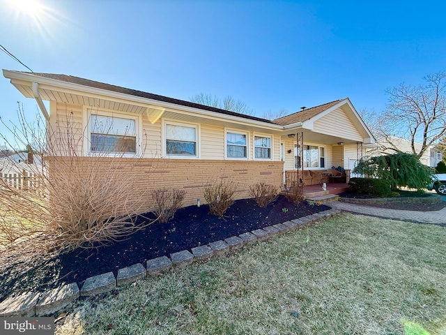 ranch-style home with brick siding, covered porch, and a front yard