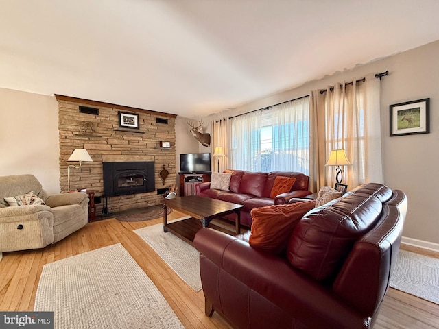 living room featuring baseboards, a stone fireplace, and light wood-style flooring