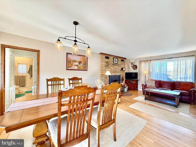 dining area with a stone fireplace and light wood finished floors