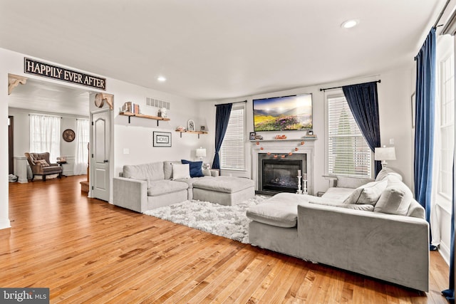 living room featuring recessed lighting, visible vents, a glass covered fireplace, and hardwood / wood-style flooring